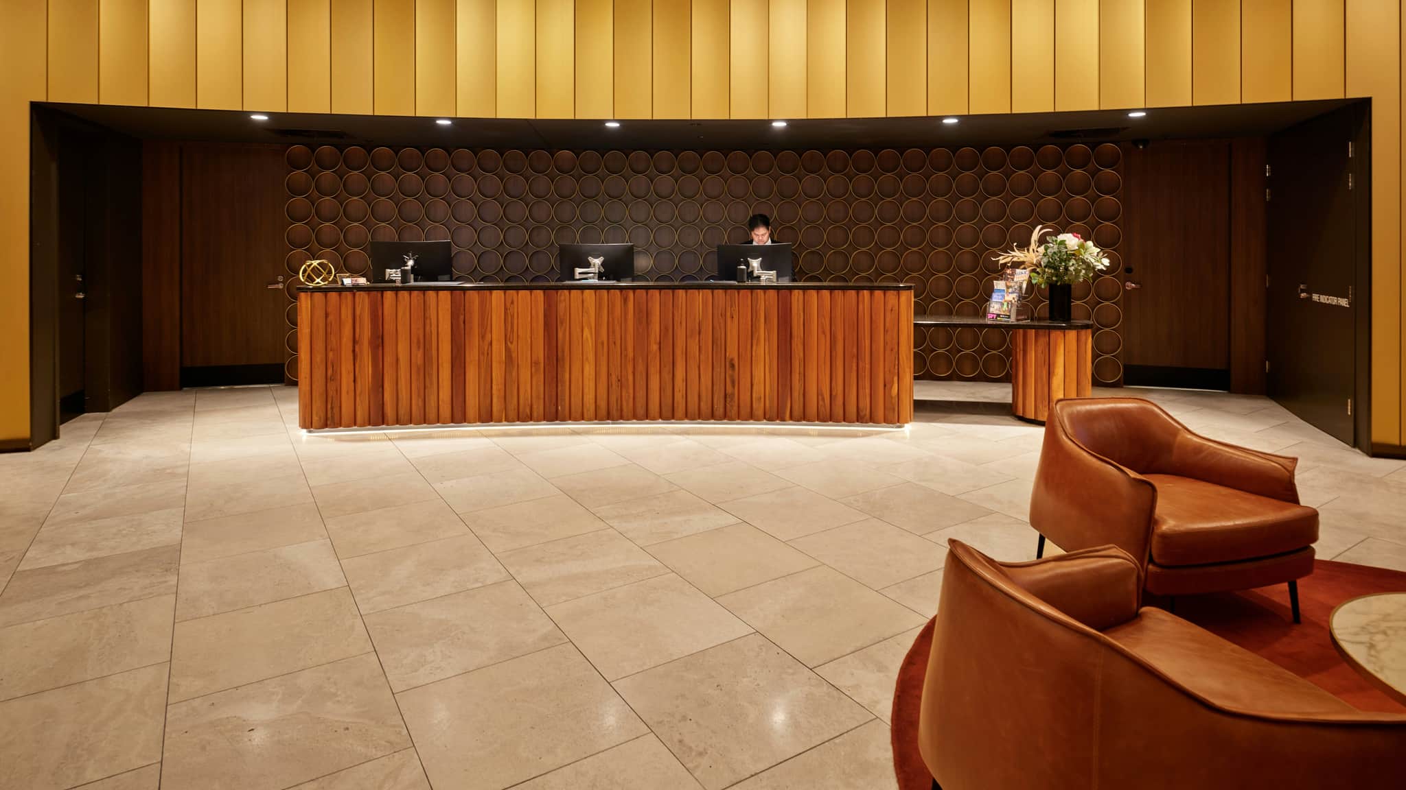 A hotel lobby with a person standing behind the desk looking downwards.