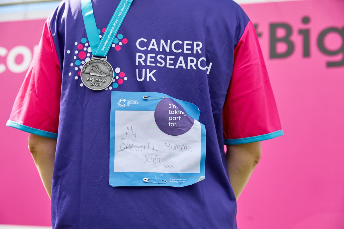 The back of a person wearing a Cancer Research UK t-shirt displaying her Big Hike medal and back sign.