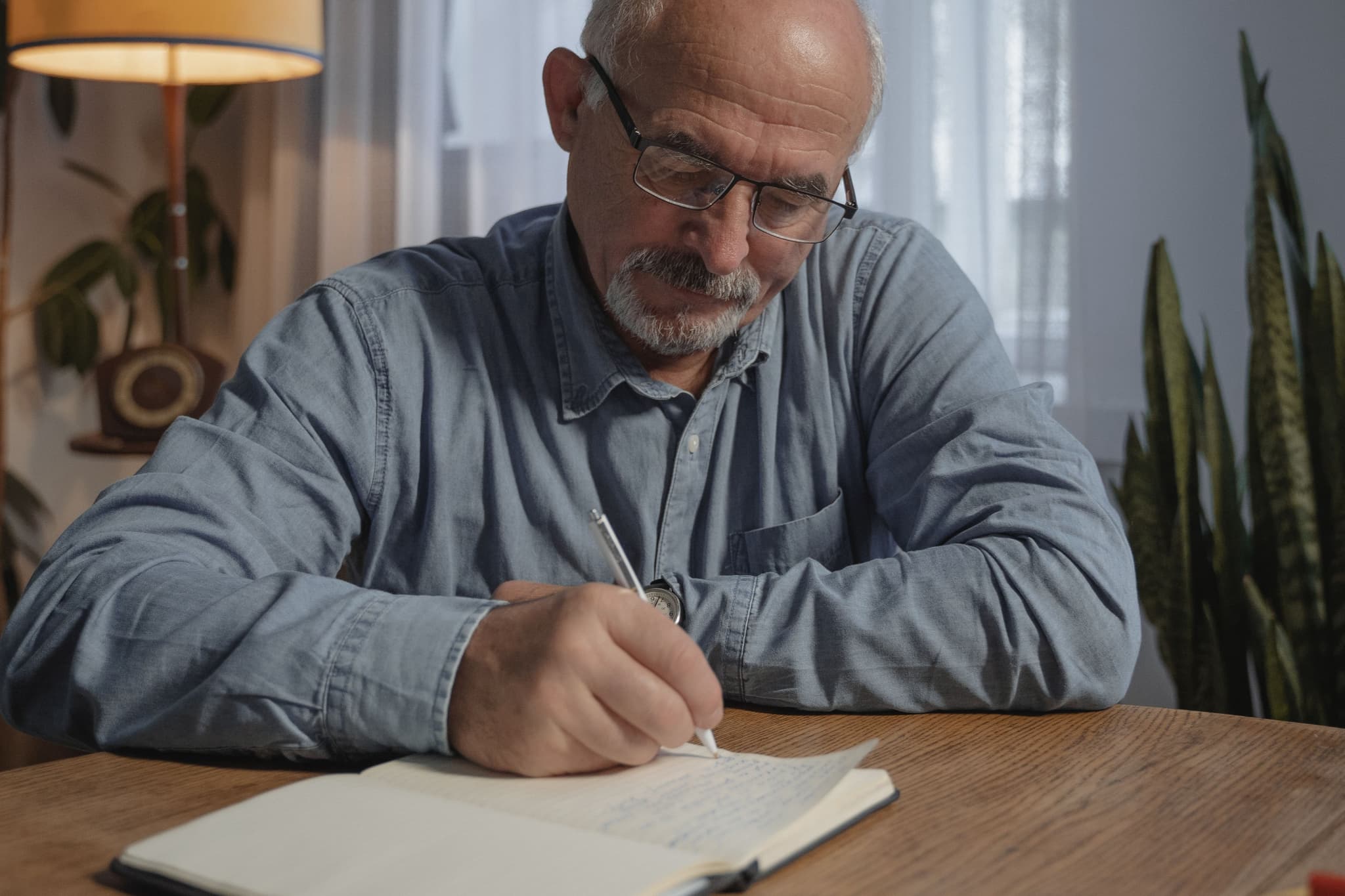 An older man sits at a table writing in a notebook.
