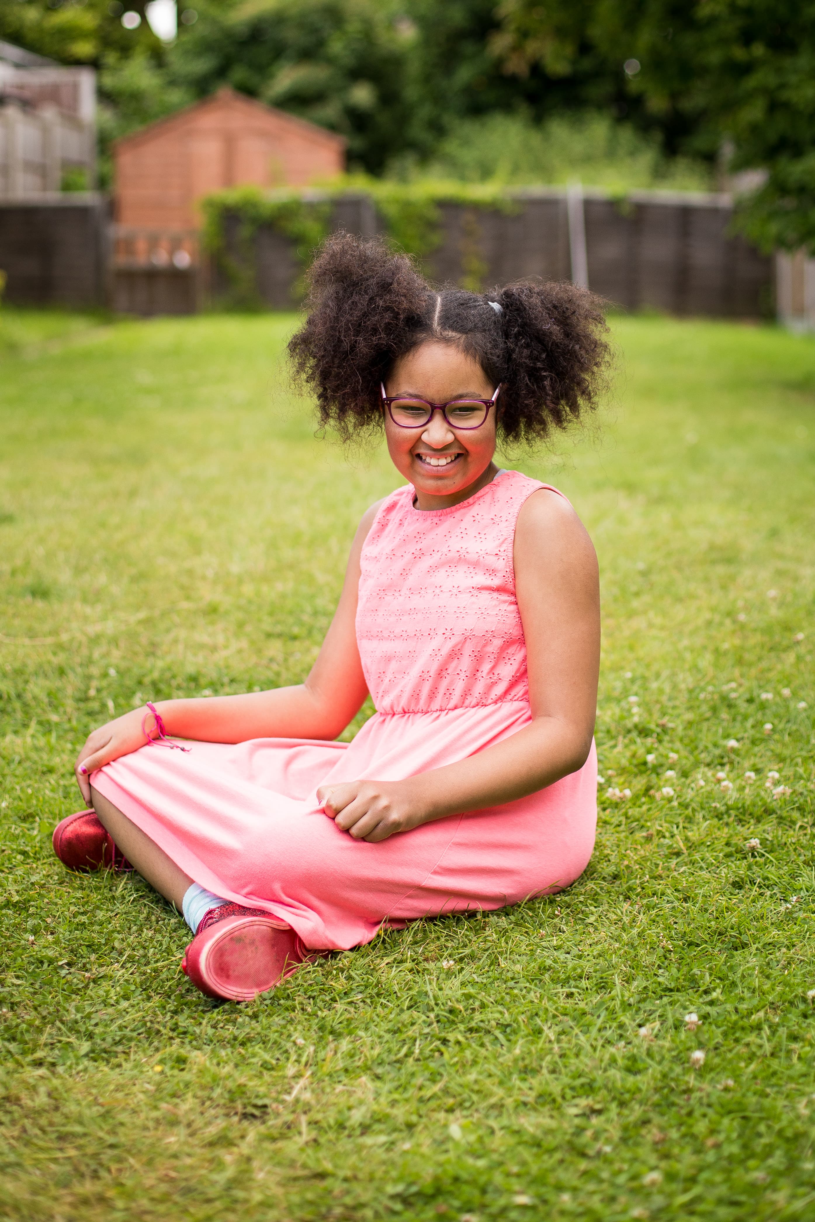 Zofeya, in remission from a brain tumour, sits cross-legged in a garden, smiling.