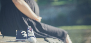 A woman holding her pregnancy bump and a pair of children's shoes