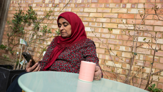 Woman sits outside with a mug looking at her phone 