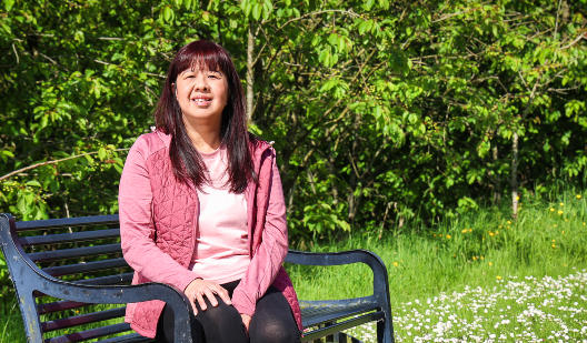 Jennifer in a pink top sitting on a bench in the woods