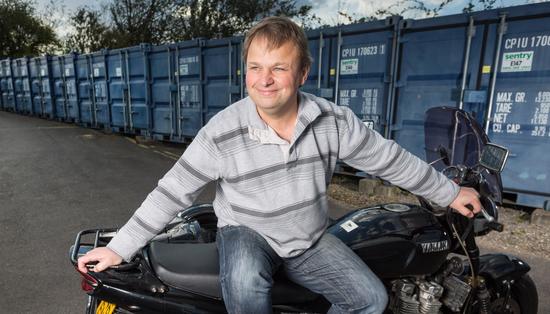 Laine smiling while sitting on his Yamaha motorbike with garages in the background