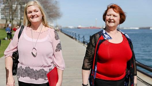 Two women walking along a river front in work clothing