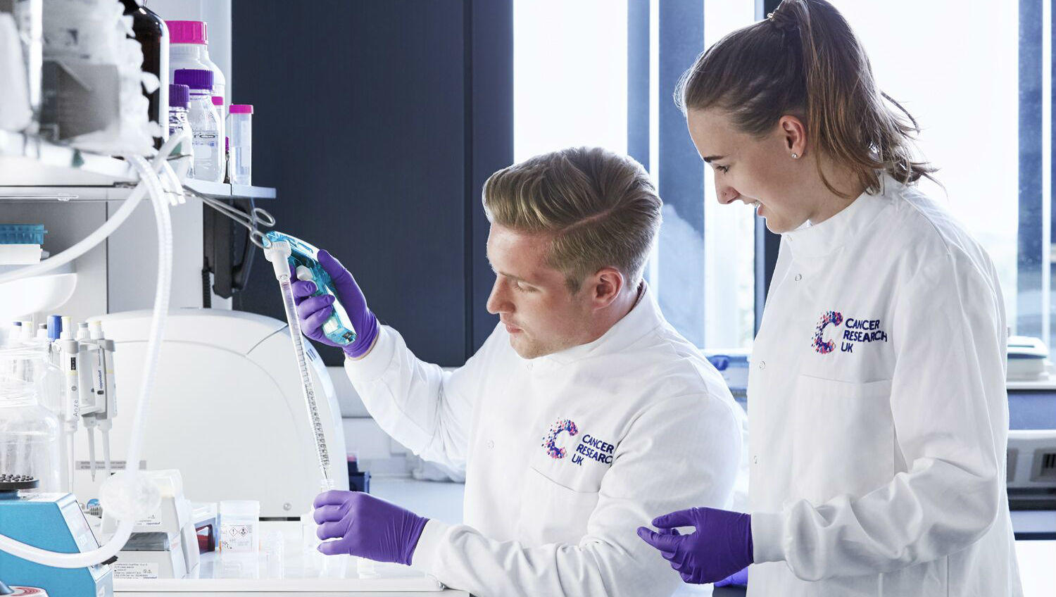 Two scientists completing an experiment in the lab Scientist in lab with PhD student looking over shoulder