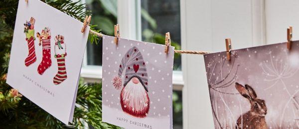 3 Christmas cards are pegged on a string by a fir tree