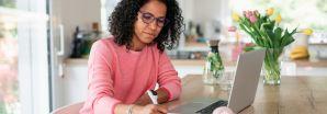 A lady with black hair wearing a pink jumper is using a laptop