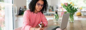 A lady with black hair wearing a pink jumper is using a laptop