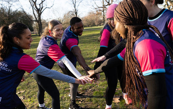 An image of a circle of people wearing Cancer Research UK t-shirts putting their hands together
