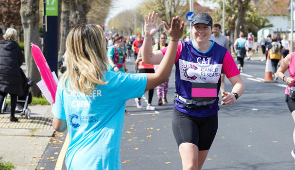 Image of supporter running in Brighton Marathon 2022. Supporter going in for a high five with a member of the volunteer crew. 