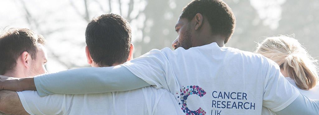 A view of the backs of four Cancer Research UK supporters with their arms around each other