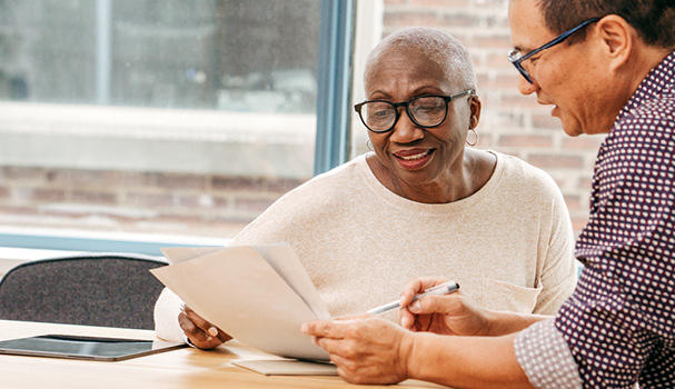 Use our Free Will Service An older lady using the free will service is sat at a table with a male solicitor updating her Will and smiling.