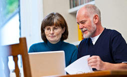 An older man is sat at the table with one of our partnered solicitors updating his Will on a laptop via the free will service.