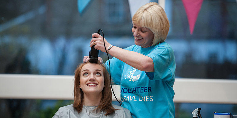 Photo of a woman getting her head shaved at a charity event