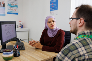 Dr talking to a patient at a desk in front of a computer 