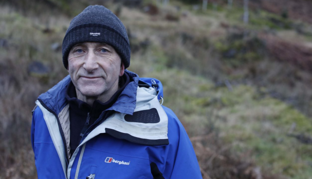 Jo, a pledger, pledges to fight cancer even when he’s gone. Jo is stood by a grassy hill wearing a warm coat and hat.