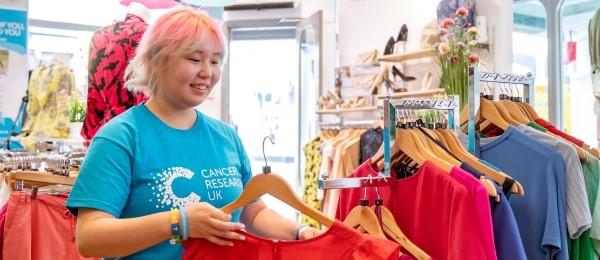 Female volunteer in CRUK shop putting a top on a clothing rail
