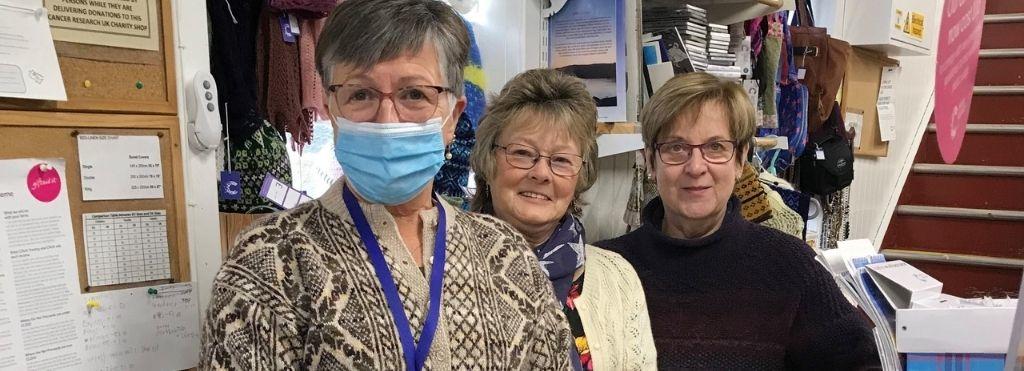 3 ladies are standing behind a till and one is wearing a face mask