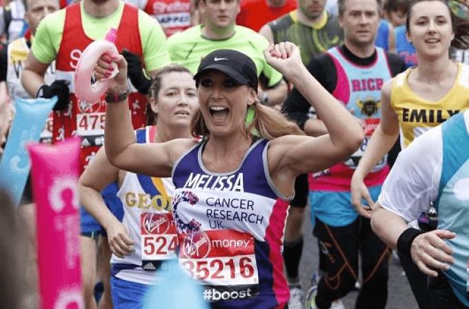 Female runner wearing a CRUK running vest smiling holding her hands in the air during the London Marathon