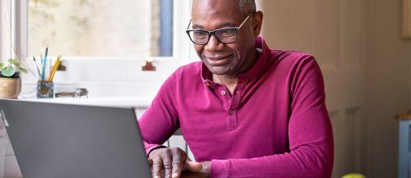 A man is working at a laptop wearing a pink jumper and glasses