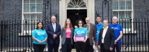 A group of people stand in front of 10 Downing Street. One holds a petition box.