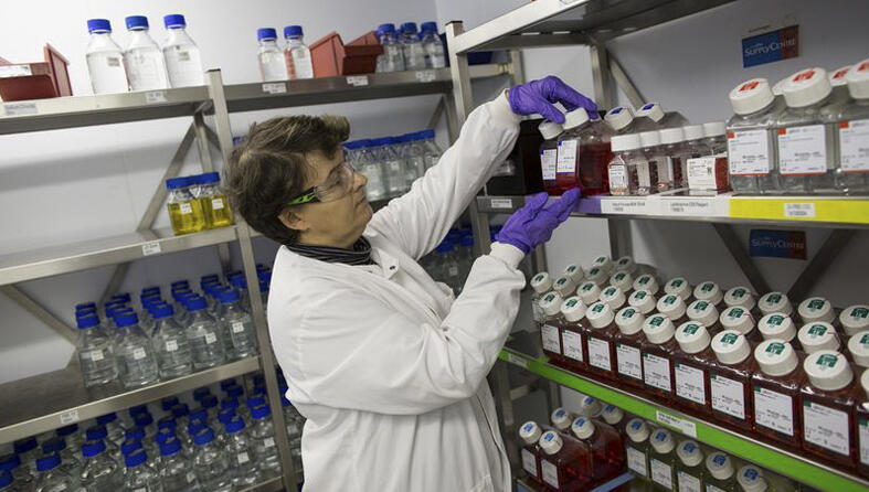 A researcher in a lab next to shelves full of samples and reagents