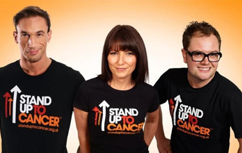 Dr Christian Jessen, Davina McCall and Alan Carr stand on an orange background wearing Stand Up To Cancer t-shirts