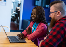 Two people sitting at a table, looking at a laptop indoor.