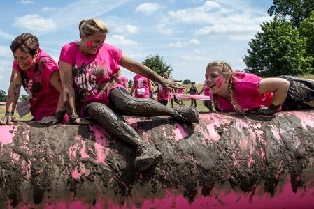 Three muddy participants climbing out of the Mud Pit at a Pretty Muddy event