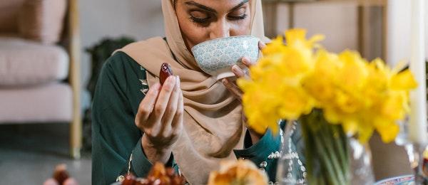 A woman in a beige hijab drinking from a bowl