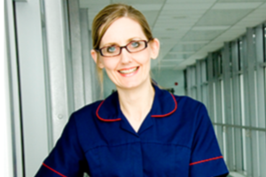 A nurse in a blue uniform smiling in a hallway