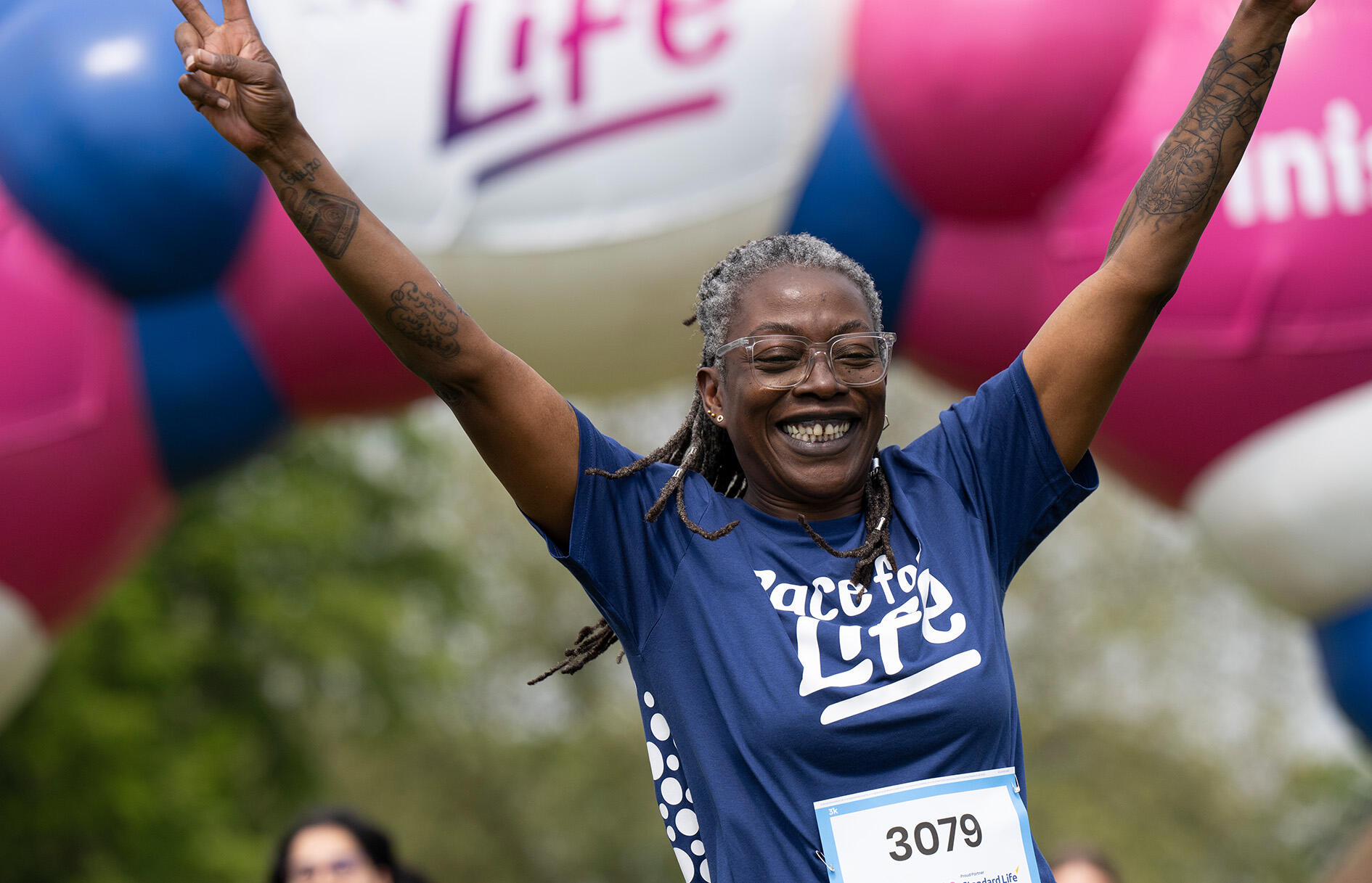 Race for Life participant celebrating with hands in the air at finish line wearing a Race for Life T-shirt