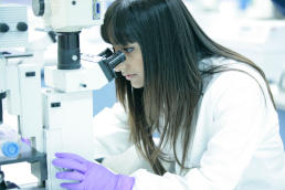 A Cancer Research UK scientist looks down her microscope