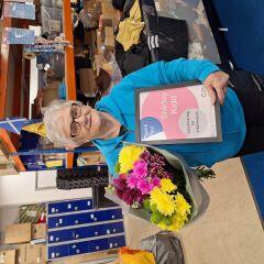 A shop volunteer who is a women smiling and holding a flower 