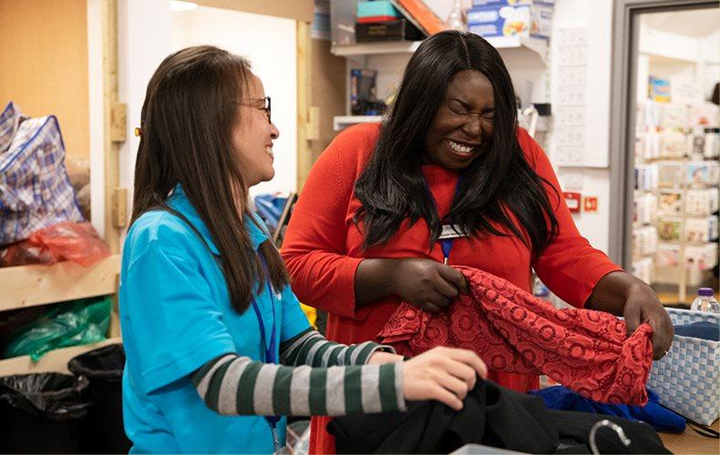 Young female volunteer laughing with a shop manager sorting clothes in a shop