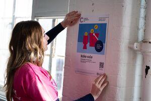 A picture of someone putting up Cancer Research UK bake sale poster