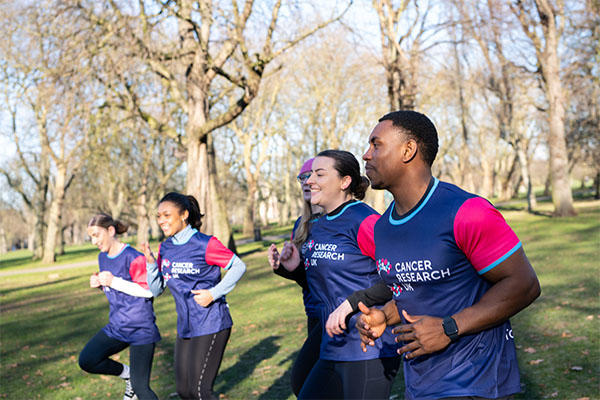 A group of runners in the park running in a line wearing CRUK tops
