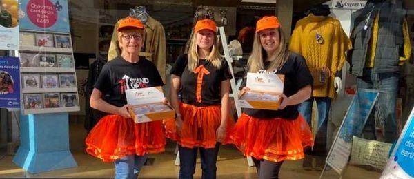 Volunteers wearing stand up to cancer tops and orange tutus