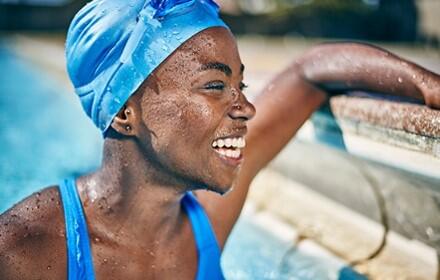 A picture of a lady in a swimming pool smiling wearing a swimming cap