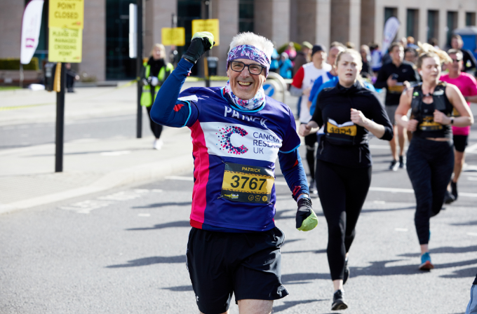 Sign up to take part in a CRUK event A man running the London Landmarks Half Marathon, he is wearing glasses, a purple bandana and he is smiling.