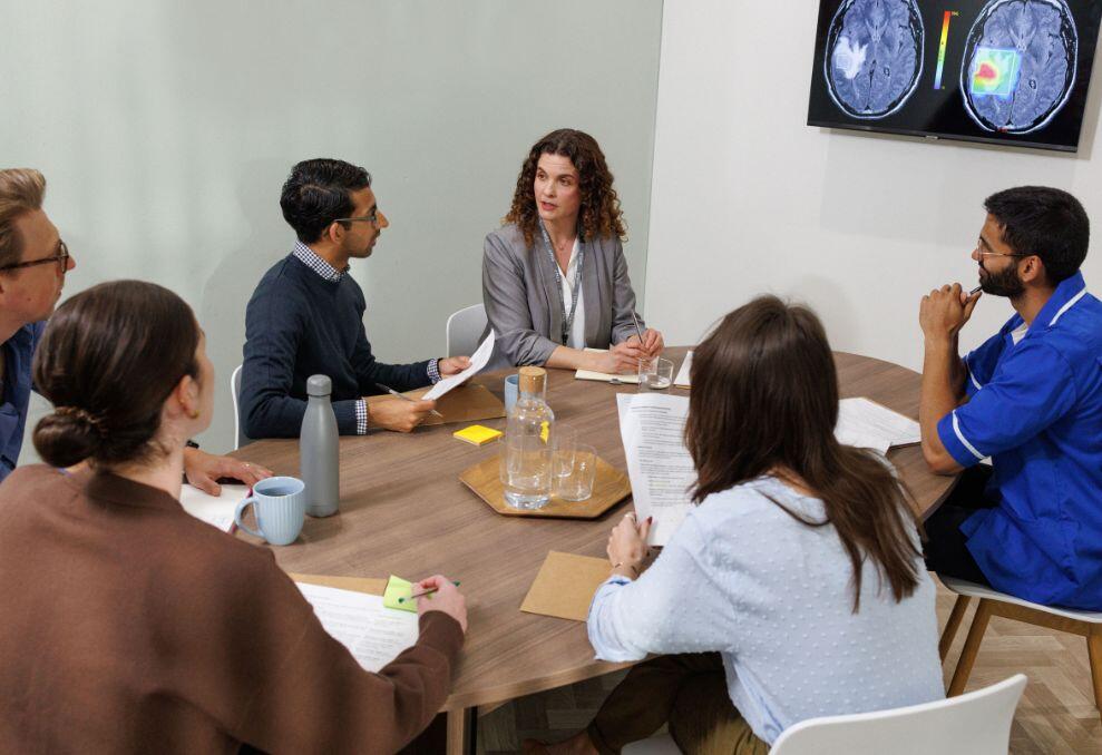 Drs sitting around a table looking at a scan on a tv screen Drs sitting around a table looking at a scan on a tv screen