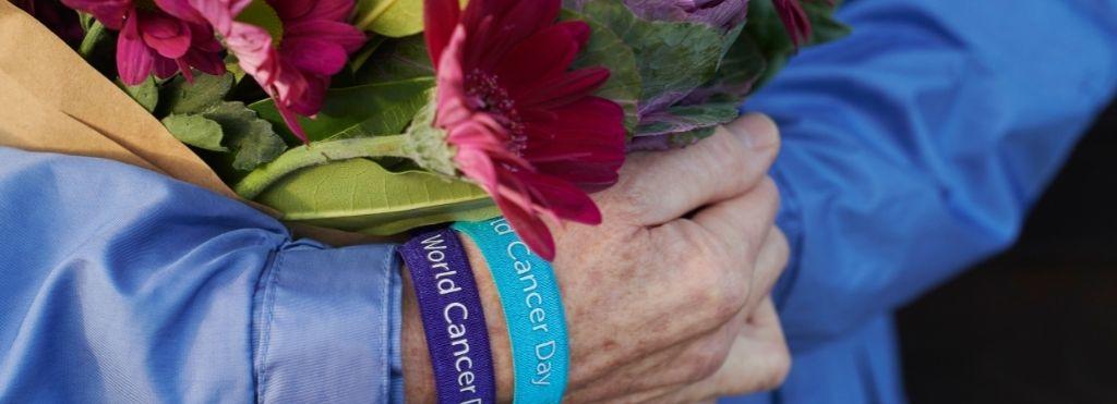 A lady is carrying a bunch of flowers and wears 2 world cancer day wristbands