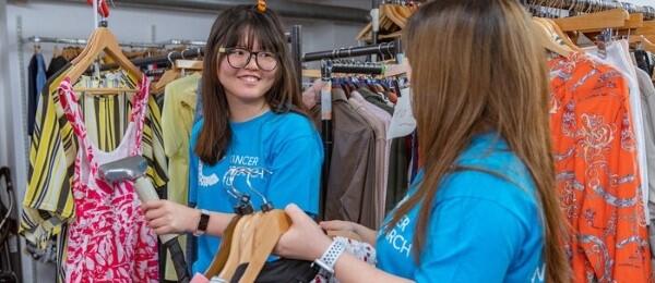 Two volunteers hanging up and sorting clothes on CRUK shop floor