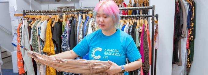 Shop volunteer in front of a rail of clothes, holding a dress