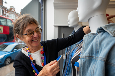 A shop volunteer smiling as they are dressing the window display mannequins