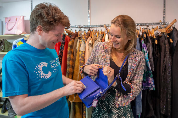Shop volunteer cheerily helping a customer look at a handbag.