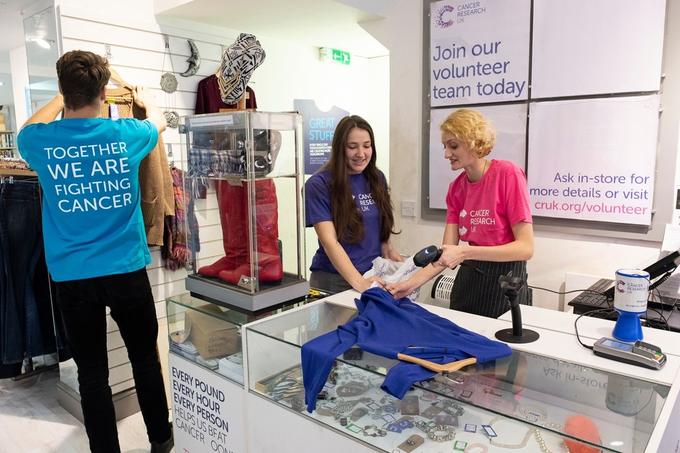 Three volunteers in a CRUK shop, working near the till