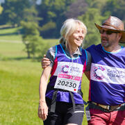 man and a woman with their arms around each other walking in the countryside