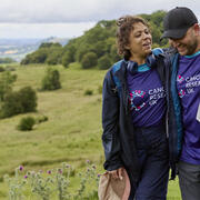 man and a woman with their arms around each other walking in the countryside
